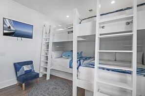 Habitación con literas, un televisor en la pared, una silla y una alfombra estampada.