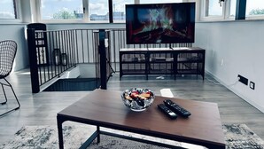 Ein modernes Wohnzimmer mit großem Fernseher, einem Essbereich und einer Treppe.