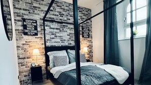 Ein modernes Schlafzimmer mit einem Himmelbett, einer Wand im Ziegelstein-Look und einem kleinen Nachttisch mit Lampe.