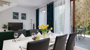 Ein Essbereich mit Tisch für vier Personen, einem Flachbildfernseher an der Wand und Blick ins Freie durch große Fenster.