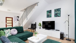 Ein modernes Wohnzimmer mit einem grünen Sofa, einem weißen Couchtisch, einem Flachbildfernseher und einer Treppe.