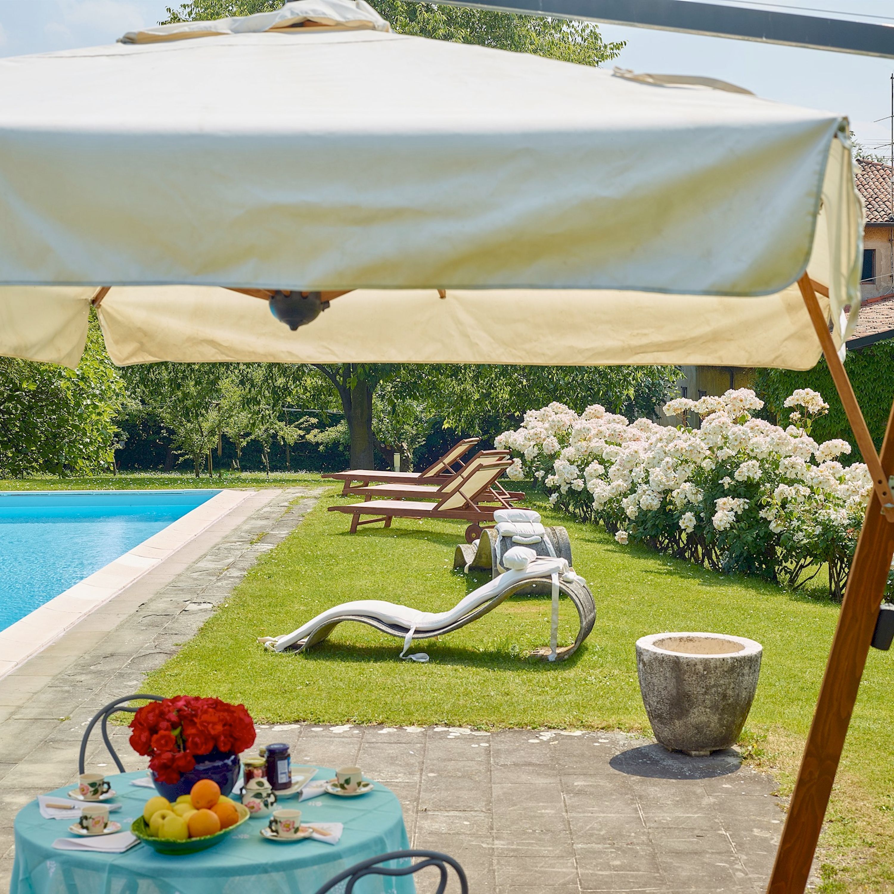 A poolside area with a lounge chair, a table with a fruit bowl, and a flower vase.