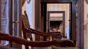 A hallway with a fireplace, wooden chairs, and a door leading to another room.