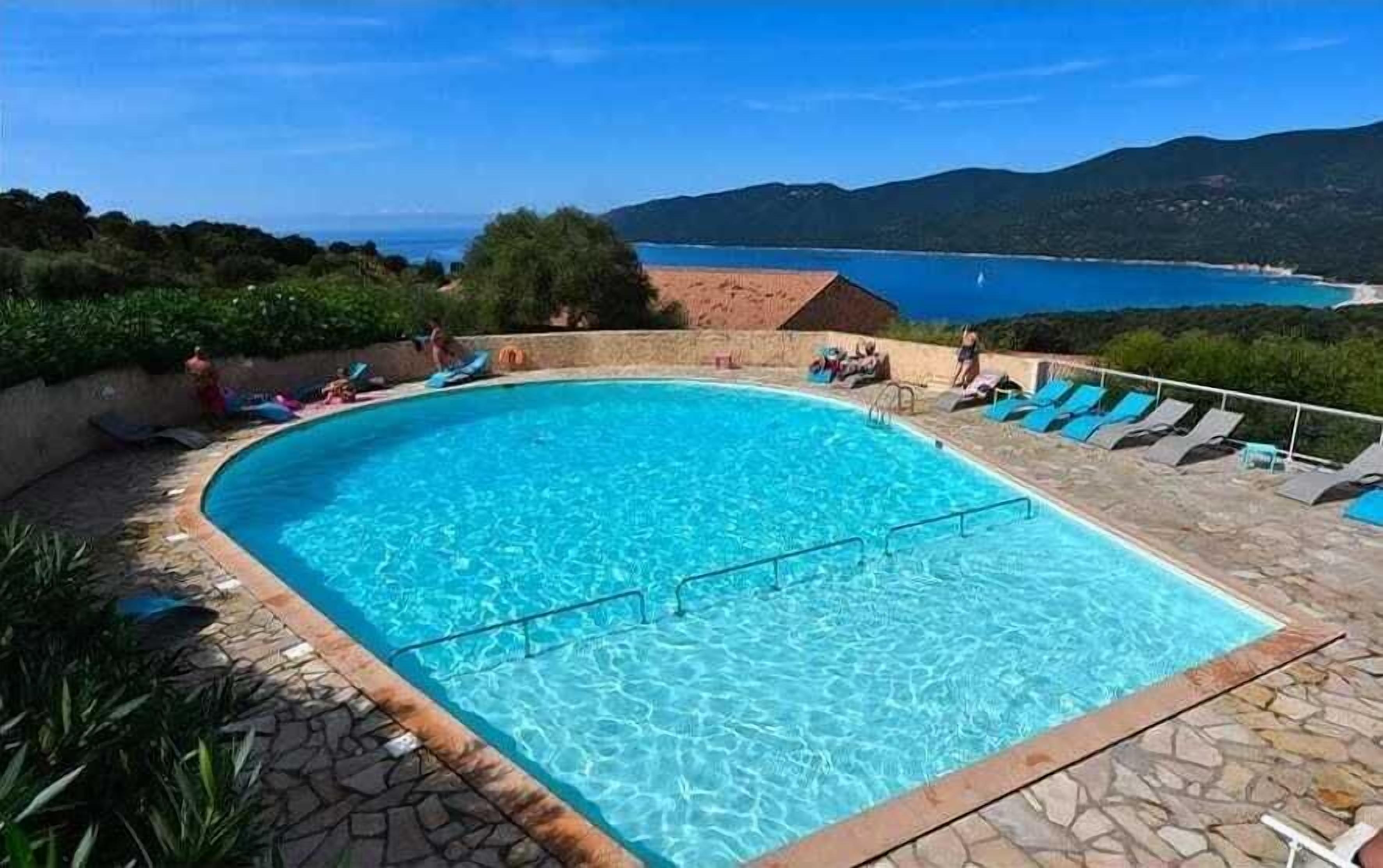 Une piscine à l’eau d’un bleu cristallin, entourée de chaises longues et d’une terrasse en pierre.