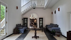 A spacious living area with a high ceiling, a staircase, and a dining area with a central tree trunk. - Villa Inlet Galle (Galle)