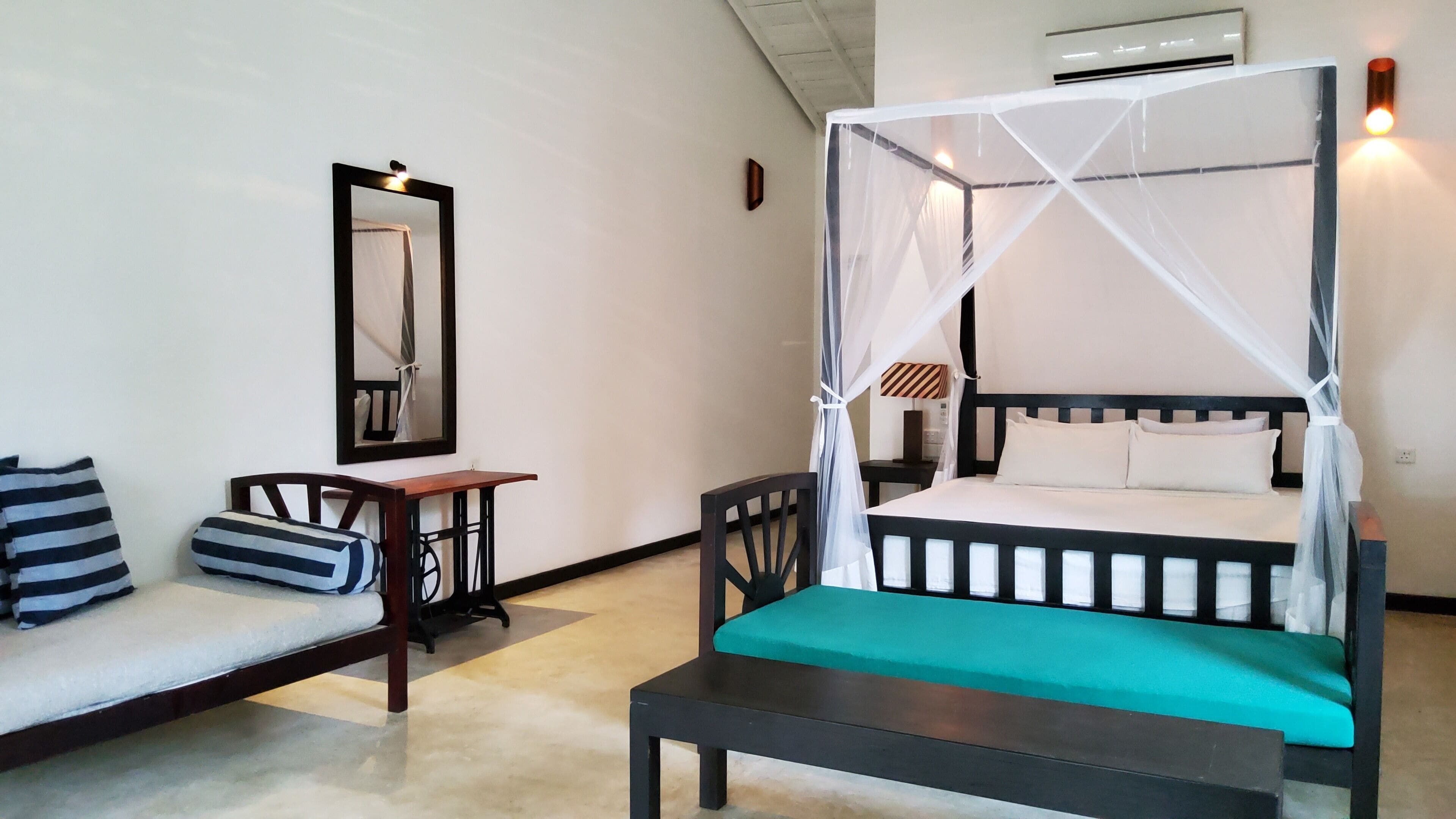 A room with a bed under a canopy, a sofa with striped pillows, a small table, and a chair.
