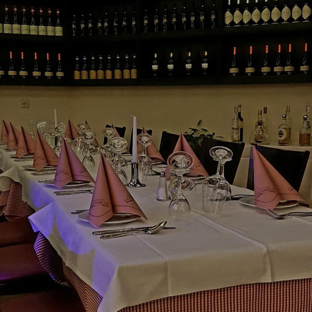 Um restaurante com mesas preparadas para refeições, cada uma com toalha branca, guardanapos cor-de-rosa e talheres.