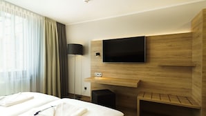 Ein Hotelzimmer mit einem Bett, einem an einer Holzplatte montierten Fernseher, einer Lampe und einem Lautsprecher.