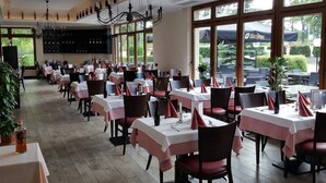 Ein Restaurant mit mehreren Tischen, jeder Tisch mit einer weißen Tischdecke und roten Servietten, und einer großen Pendelleuchte an der Decke.