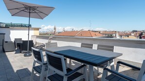 Terraço no telhado com mesa, cadeiras, um guarda-sol e vista para a cidade.