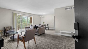 Un salon moderne comprenant un canapé, un fauteuil, une table basse en verre et un coin repas avec une table et des chaises.
