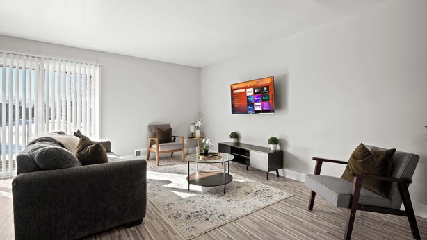 A modern living room with a sofa, armchairs, a coffee table, and a flat-screen TV mounted on the wall. - Stylish & Modern Unit  Prime Location & Comfort (Rochester Hills)