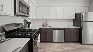 A modern kitchen with stainless steel appliances, white cabinets, and a wooden floor. - Stylish & Modern Unit  Prime Location & Comfort (Rochester Hills)