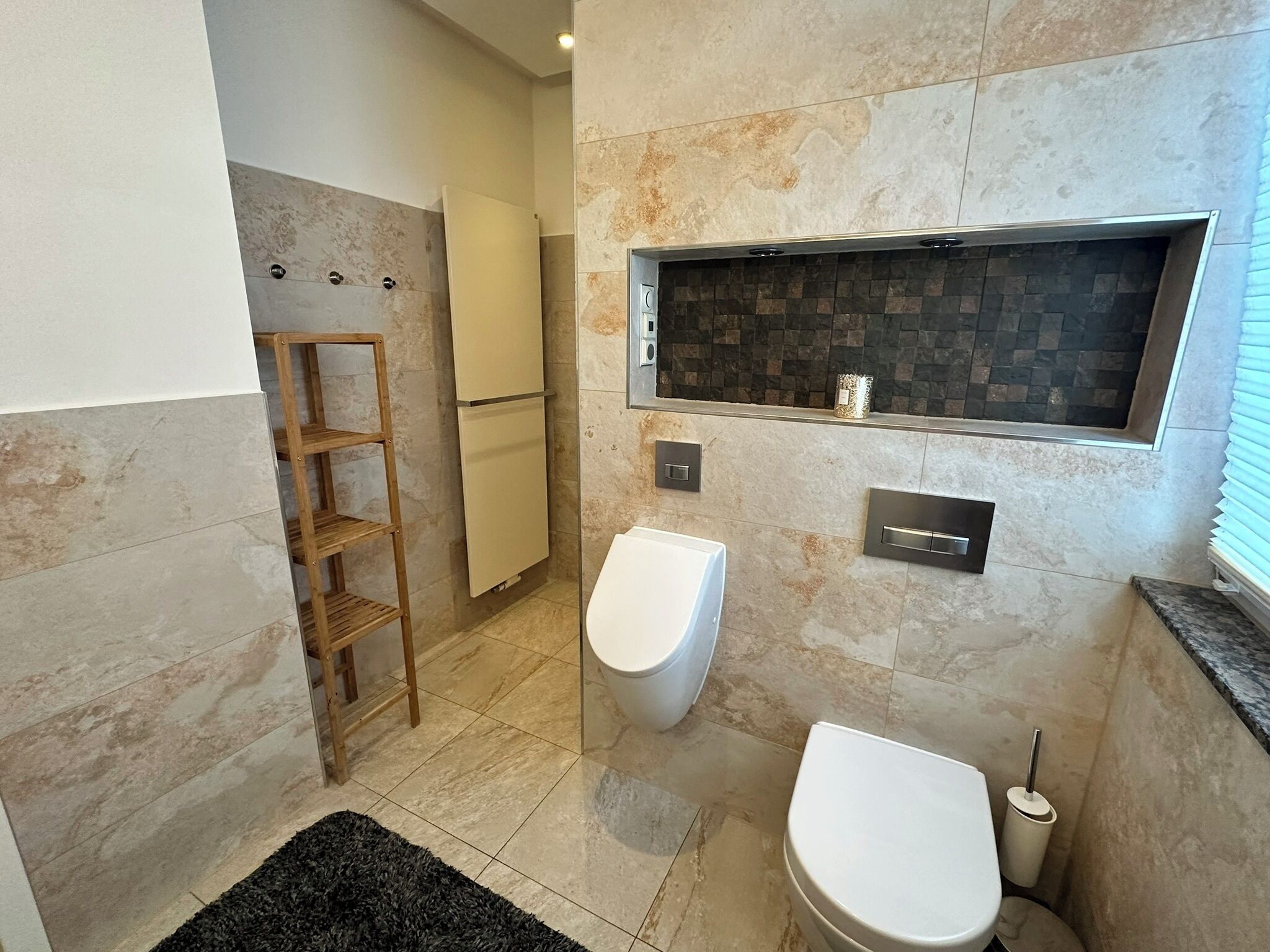 A modern bathroom with a toilet, bidet, and a shelf unit.