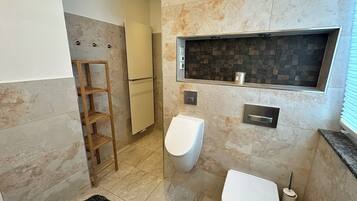 A modern bathroom with a toilet, bidet, and a shelf unit.