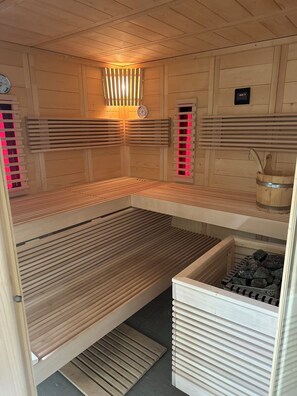 A sauna room with wooden benches, a clock, and a sauna control panel.