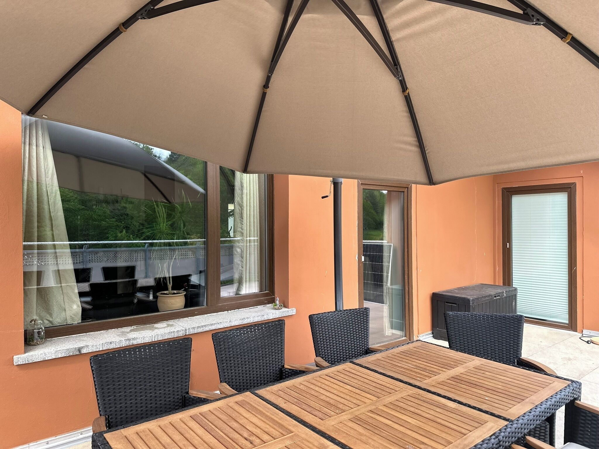 Een terras buiten met een tafel en stoelen, een grote parasol, en uitzicht op de omgeving.
