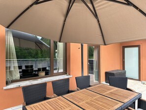 An outdoor patio with a table and chairs, a large umbrella, and a view of the outdoors.