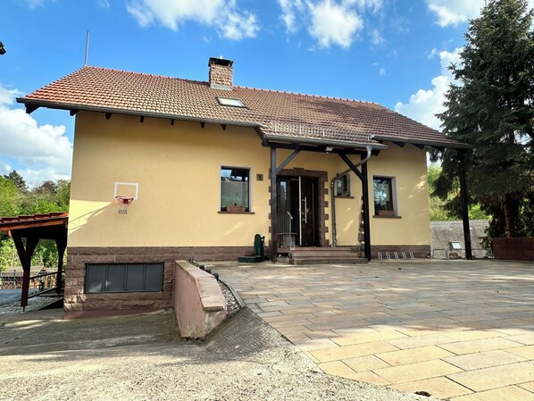 A two-story house with a tiled roof, a small porch, and a basketball hoop.