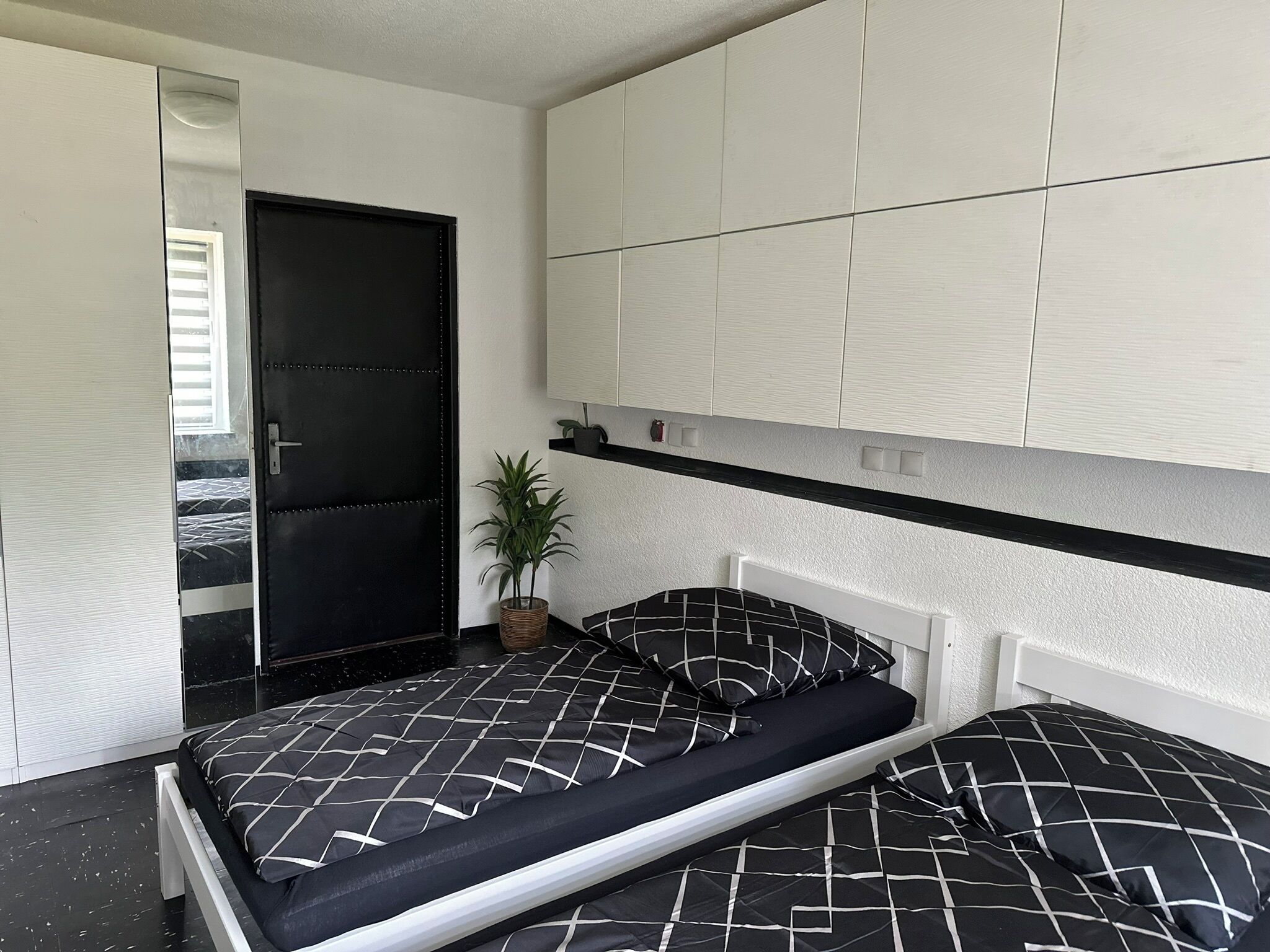 Ein modernes Schlafzimmer mit einem schwarz-weißen Karottenbett, einem weißen Kopfteil und einer schwarzen Tür.
