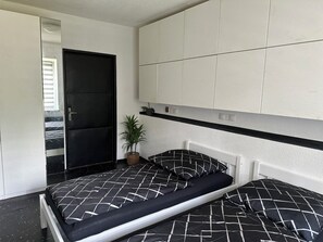 Une chambre à coucher moderne avec une couvre-lit à carreaux noirs et blancs, une tête de lit blanche et une porte noire.