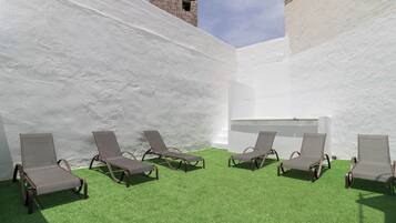 Zona exterior soleada con césped artificial y seis sillones de descanso dispuestos en semicírculo.