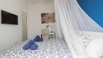 Un dormitorio con cama, una silla, un escritorio, un televisor y un adorno en la pared.