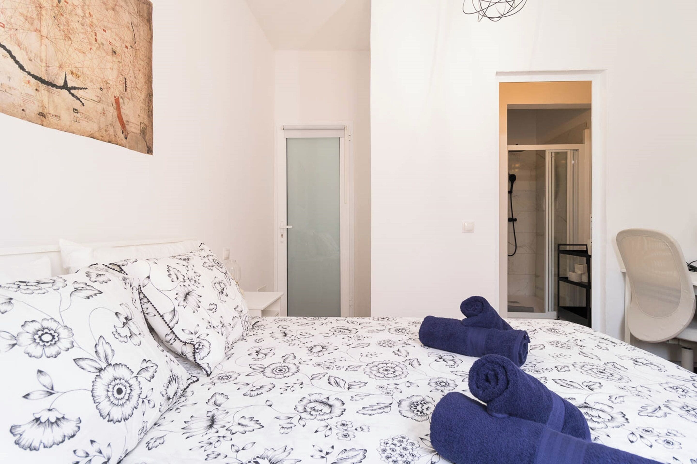 Une chambre d’hôtel avec un lit, une chaise et une salle de bain, visibles à travers une porte ouverte.