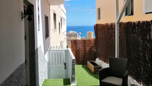 A narrow balcony with a view of the sea, a white gate, a wicker chair, and a wooden crate. - La Bussola (Las Palmas de Gran Canaria)