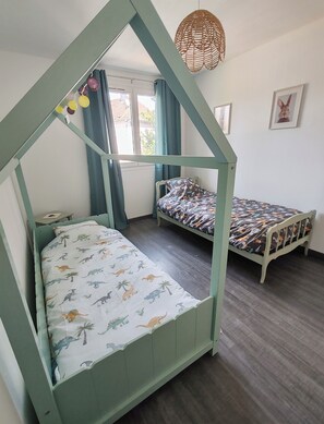 A room with two bunk beds, a window with curtains, a hanging light fixture, and a framed picture on the wall.