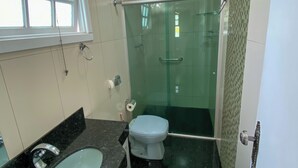 Et badeværelse med en brusekabine med glasvægge, en vask med marmorplade og et toilet.