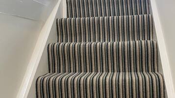 A staircase with striped carpet leading to a kitchen area.