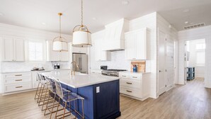 A modern kitchen with white cabinetry, a central island with bar stools, stainless steel appliances, and pendant lighting. - Luxurious Getaway in CS South with access to 20+ resort like amenities (Port Aransas)