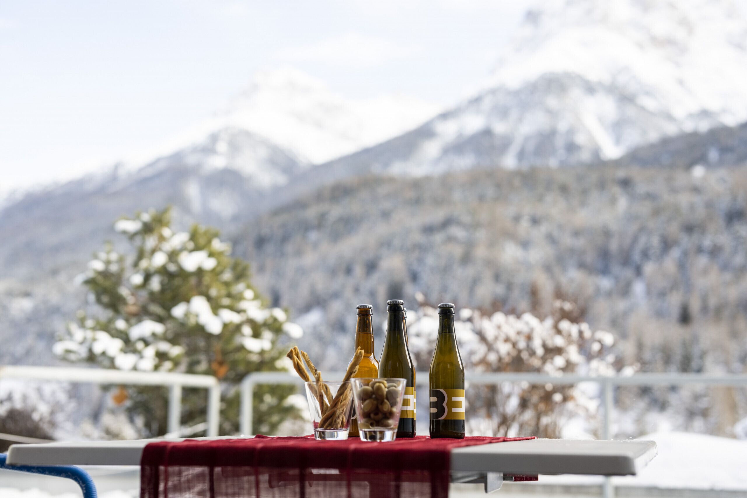 A table with bottles and snacks against a snowy mountain backdrop.