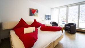 A modern bedroom with a large bed, red pillows, a wooden headboard, a black chair, and a painting on the wall. - CHASA TULAI F83: BEAUTIFULLY RENOVATED STUDIO IN HOLIDAY PARK TULAI F83 (Scuol)