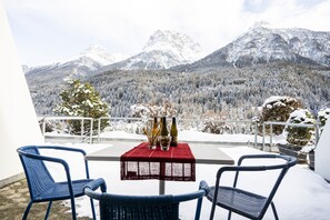 Un balcon avec une table dressée pour deux personnes, offrant une vue sur des montagnes enneigées.