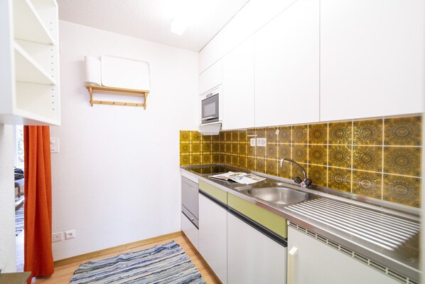Una cocina compacta con armarios blancos, un lavamanos de acero inoxidable y azulejos decorativos en el fondo.