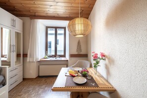 A cozy kitchen with wooden cabinets, a dining table set with food, a hanging light fixture, and a window with curtains. - Chasa Vi Studio: located in the center of Scuol (Scuol)