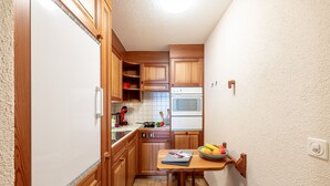 A compact kitchen with wooden cabinets, a microwave, and a small dining table with a bowl of fruit. - Chasa Vi Studio: located in the center of Scuol (Scuol)