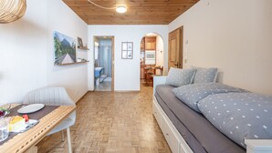 A cozy room with a wooden ceiling, a bed with polka dot bedding, a dining table with a plate and utensils, and a kitchen in the background. - Chasa Vi Studio: located in the center of Scuol (Scuol)