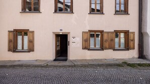 A building with a beige facade, multiple wooden-framed windows, and a cobblestone street. - Chasa Vi Studio: located in the center of Scuol (Scuol)