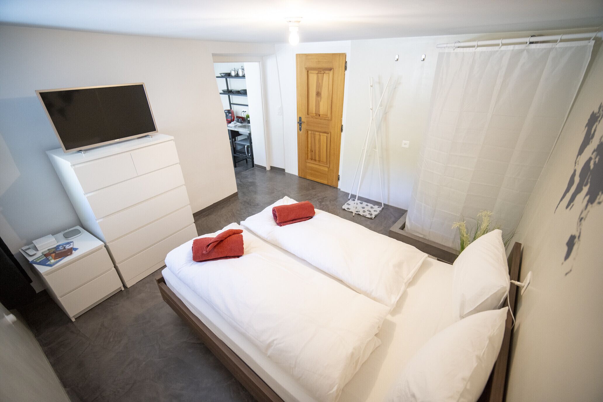 A hotel room with a bed, a TV on a dresser, a door, and a curtain.