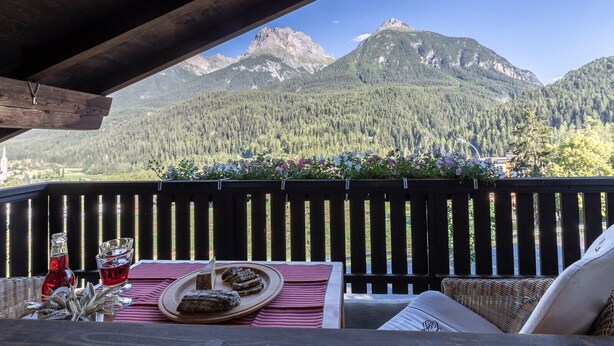 Un balcon avec une balustrade en bois, une table avec une assiette de nourriture et des boissons, et une vue sur une chaîne de montagnes.