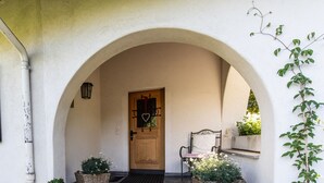 Un bâtiment blanc avec une entrée en arc de cercle, une porte en bois et un banc à l’extérieur.