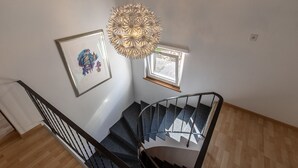 Un escalier avec une rampe noire, un plancher en bois, un tableau encadré et un luminaire suspendu.