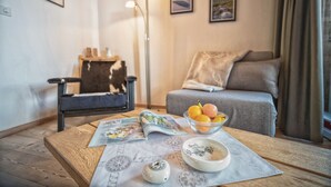 A cozy living room with a sofa, a coffee table with a bowl of fruit, a lamp, and framed pictures on the wall. - CHASA GISEP STUDIO: HOLIDAYS IN SCUOL, THAT MEANS RELAXATION IN A TYPICAL ENGADIN VILLAGE! (Scuol)