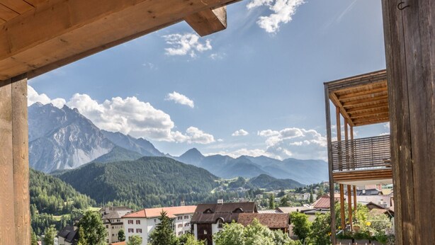 A wooden balcony overlooking a mountainous landscape with a village below. - CHASA GISEP STUDIO: HOLIDAYS IN SCUOL, THAT MEANS RELAXATION IN A TYPICAL ENGADIN VILLAGE! (Scuol)