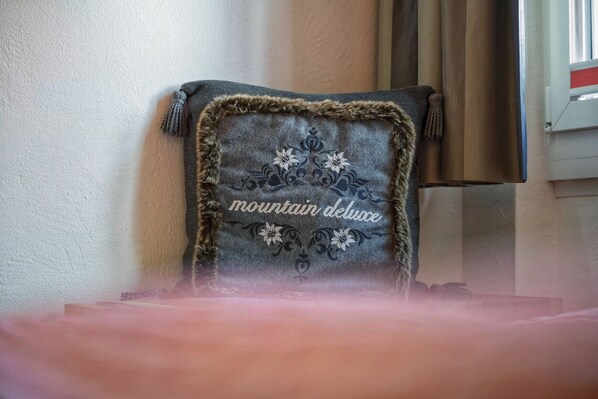 A chair with a decorative pillow featuring floral embroidery and the text "mountain delight." - CHASA GISEP STUDIO: HOLIDAYS IN SCUOL, THAT MEANS RELAXATION IN A TYPICAL ENGADIN VILLAGE! (Scuol)