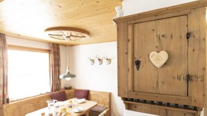 A wooden dining area with a table set for two, a bench, and a wall-mounted cabinet with a heart-shaped decoration.
