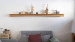 A living room with a grey sofa, a wooden shelf with decorative items, and a small table with a bowl and remote controls.